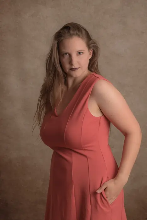 Frau im korallfarbenen Kleid beim Portrait & Fashion Fotoshooting mit klassischem Hintergrund im Fotostudio